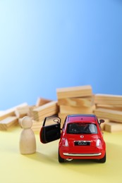 Photo of Overcoming barries for development and success. Wooden human figure near red toy car in front of blocks on yellow surface, space for text.