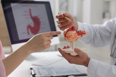 Photo of Gastroenterologist with human stomach model consulting patient at table in clinic, closeup