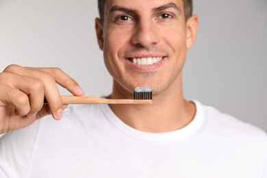 Photo of Man holding toothbrush with paste on light background, closeup