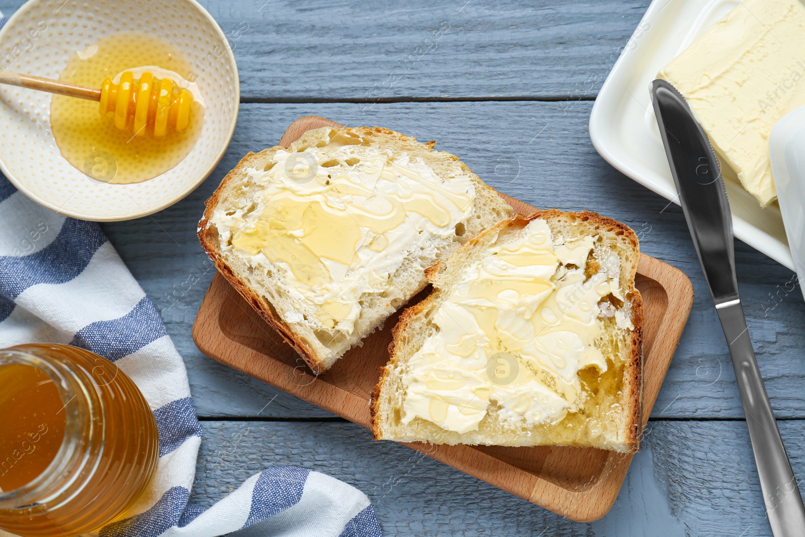 Photo of Slices of bread with butter and honey on grey wooden table, flat lay