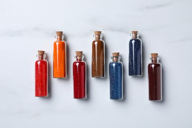 Glass bottles with different food coloring on white marble table, flat lay