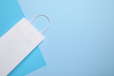Photo of White paper bag on light blue background, top view. Space for text