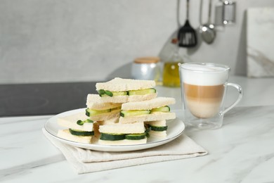 Photo of Tasty sandwiches with cucumber, butter, microgreens and coffee on white marble table in kitchen, closeup