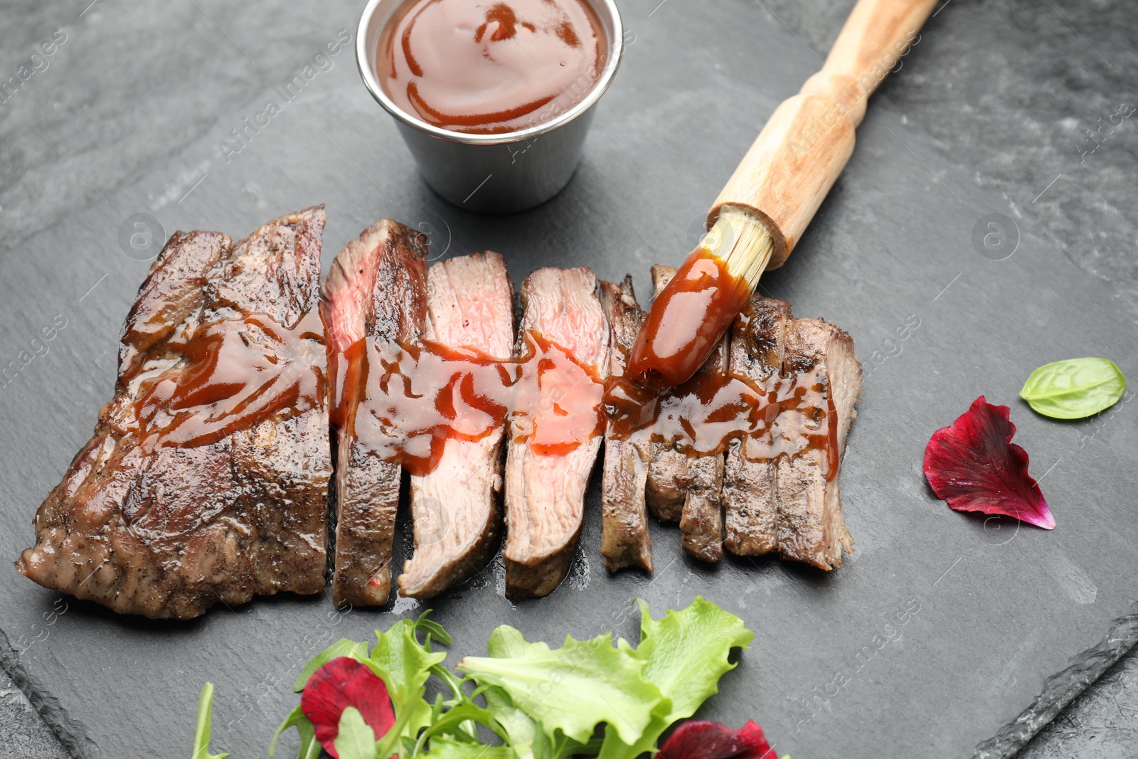 Photo of Pieces of delicious roasted beef meat with sauce and greens on black table, closeup