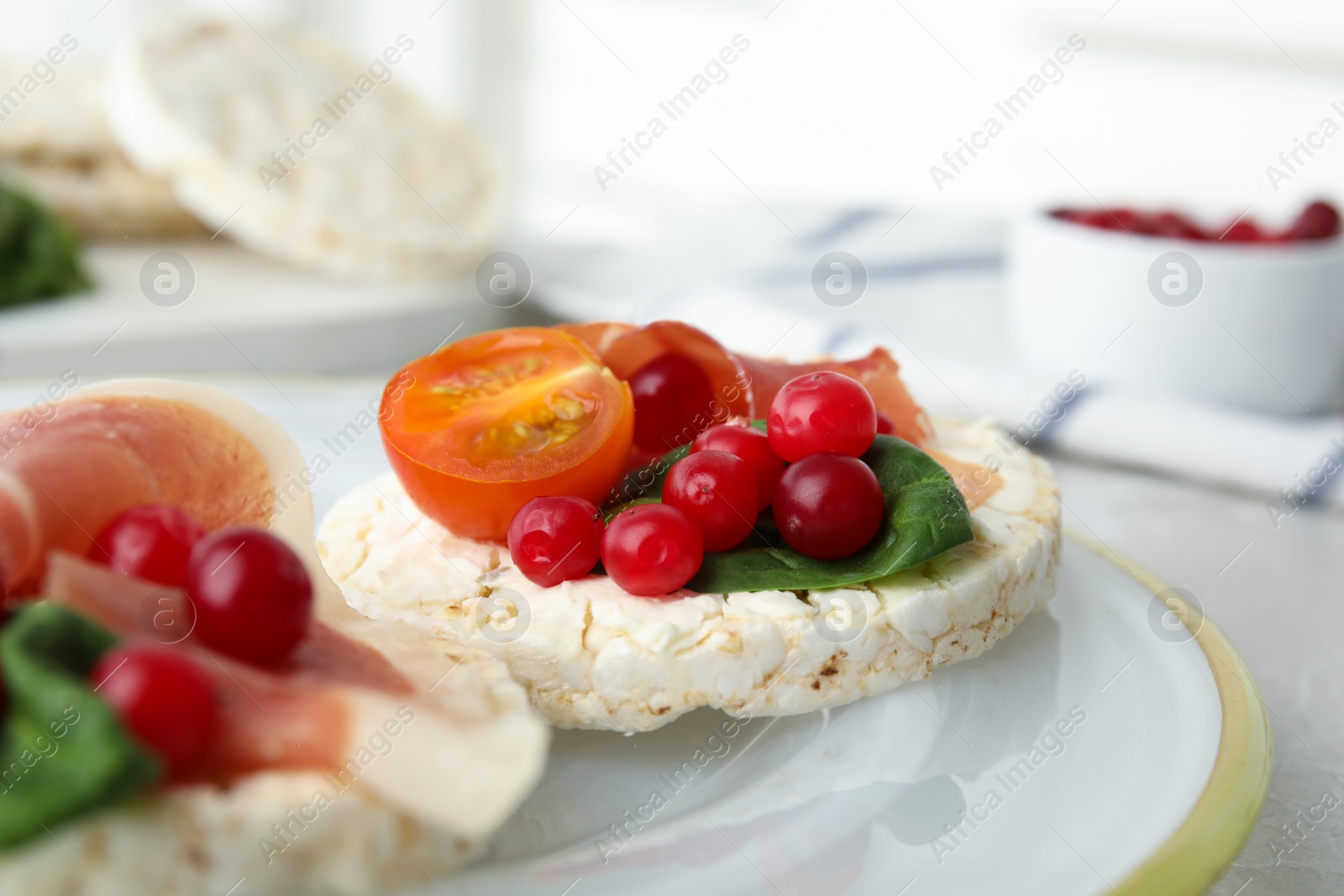 Photo of Puffed rice cakes with prosciutto, berries and basil on plate, closeup