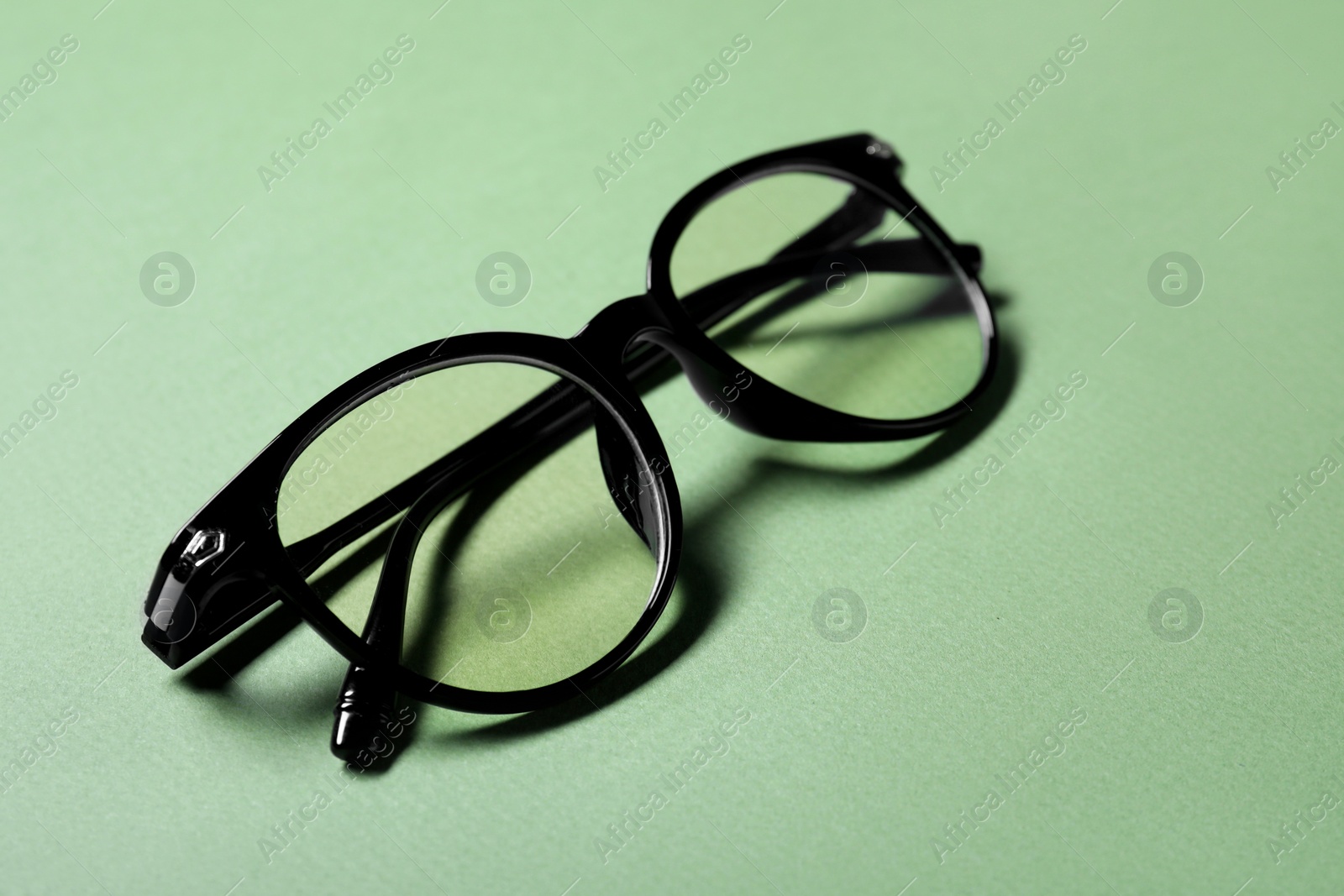 Photo of Stylish pair of glasses with black frame on light green background, closeup