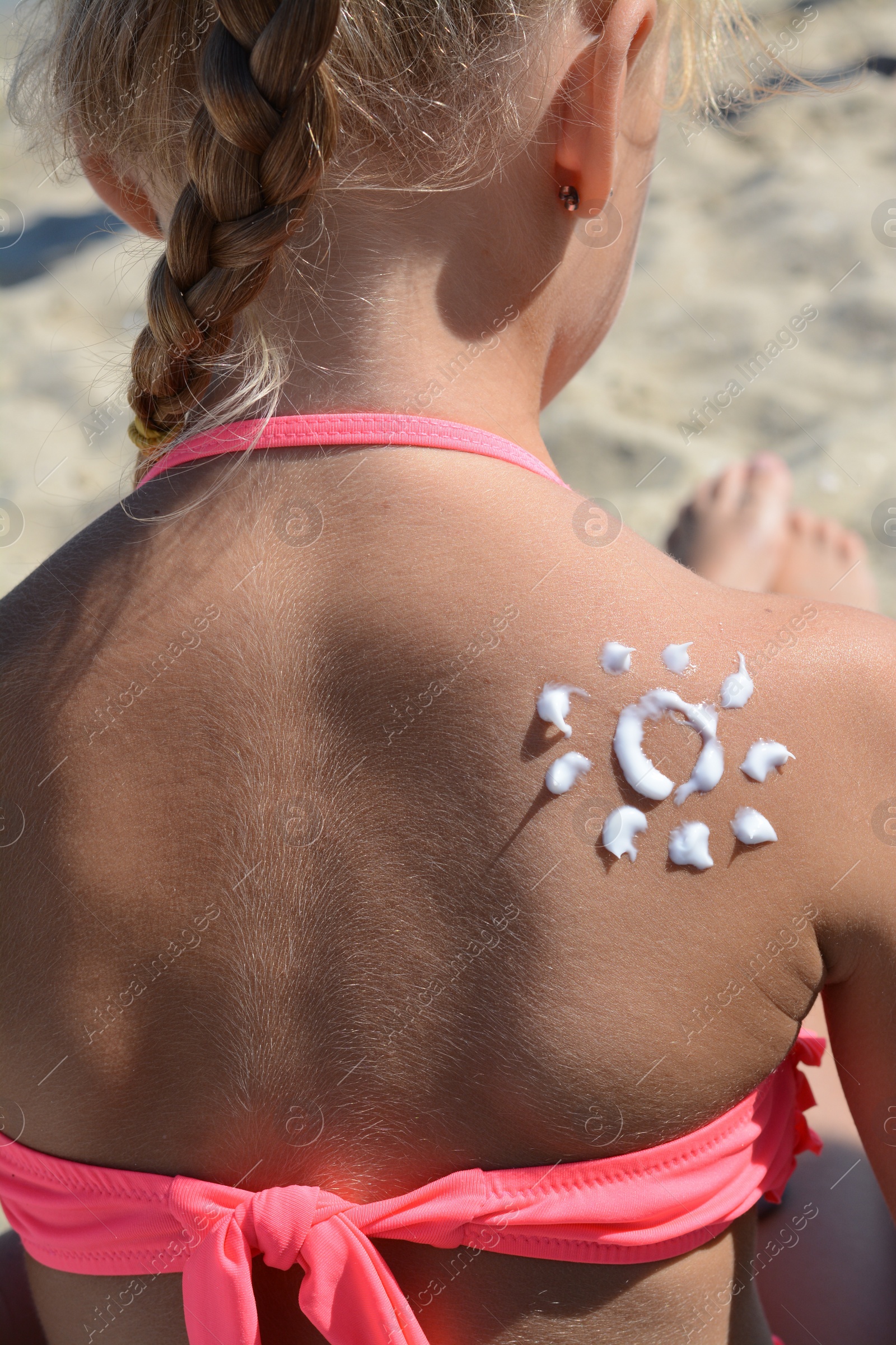 Photo of Little girl with sun protection cream on body outdoors, closeup