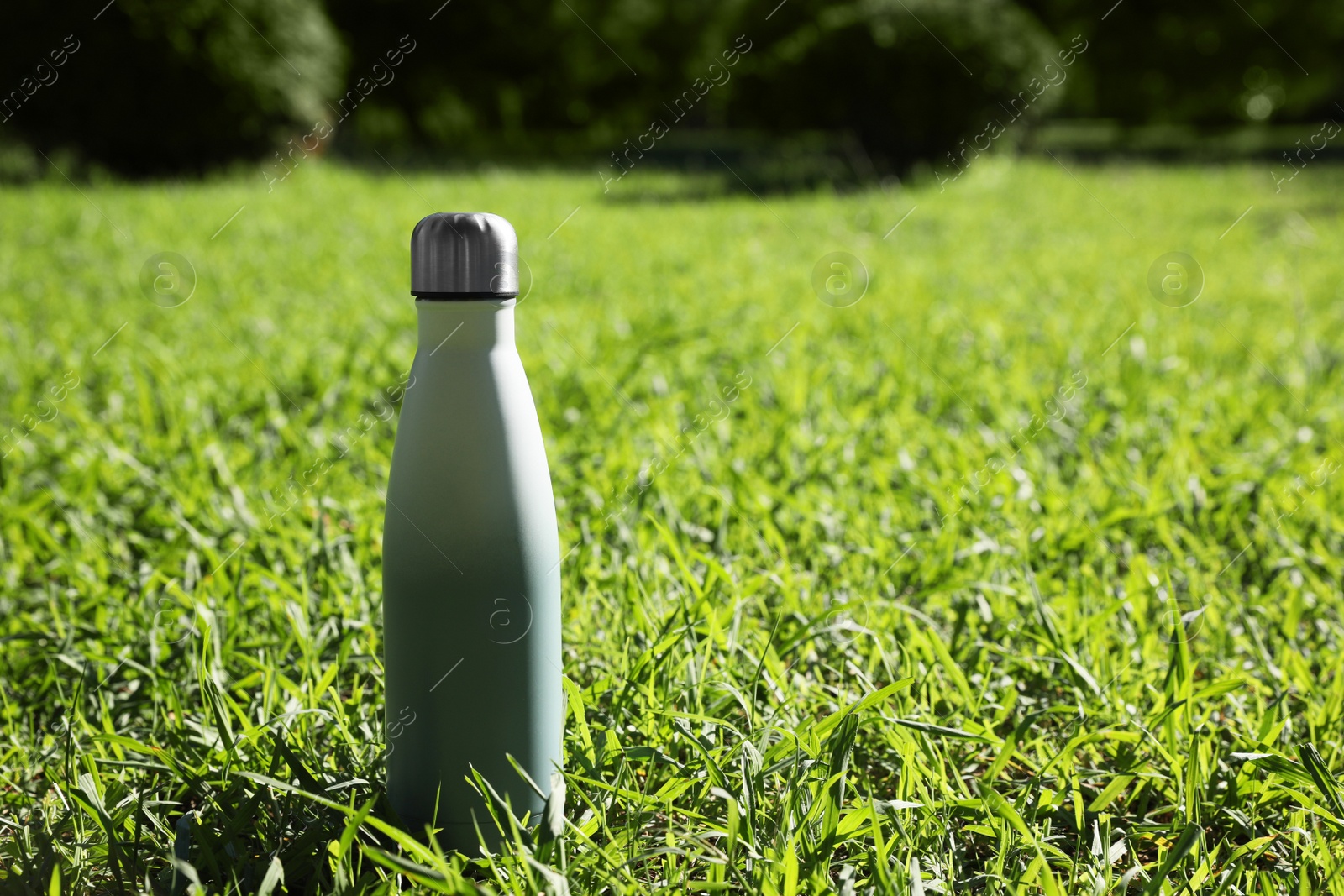 Photo of Thermo bottle on green grass in park, space for text