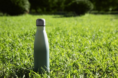 Thermo bottle on green grass in park, space for text