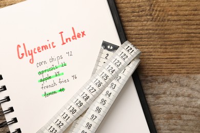 Photo of Glycemic Index. Notebook with information and measuring tape on wooden table, top view