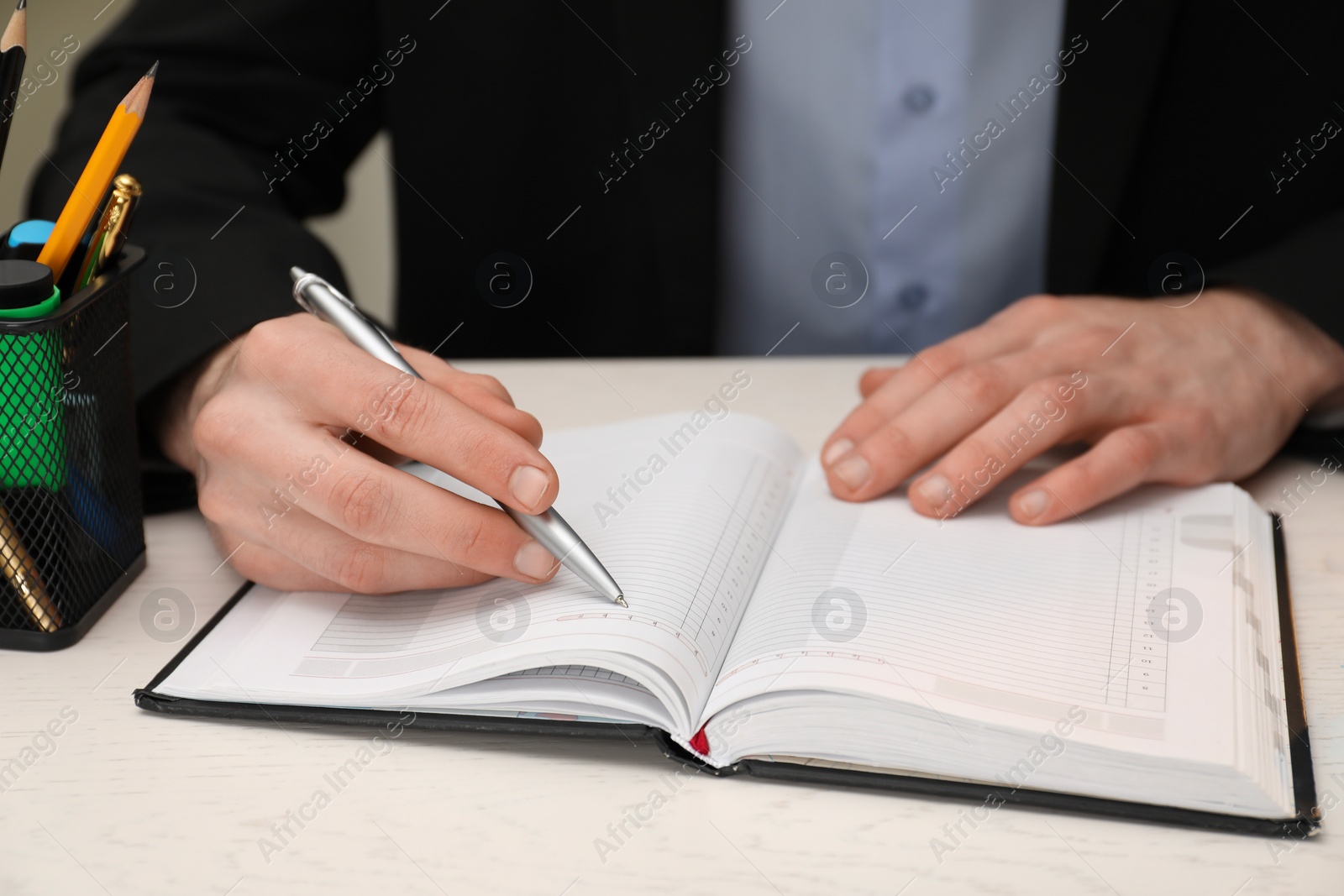 Photo of Man taking notes at white wooden table, closeup