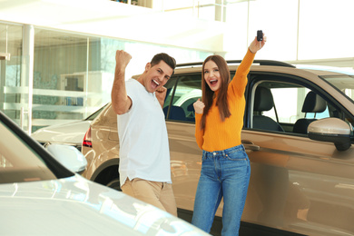 Happy couple with car key in modern auto dealership