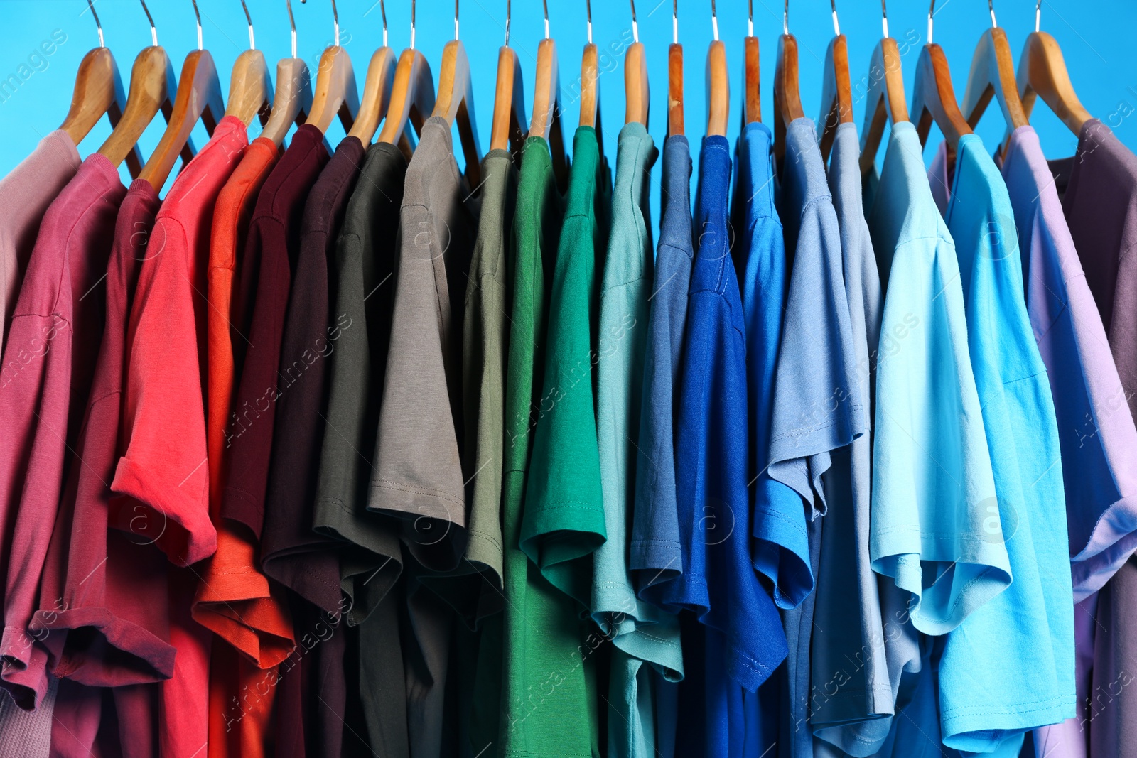 Photo of Colorful clothes on hangers against light blue background