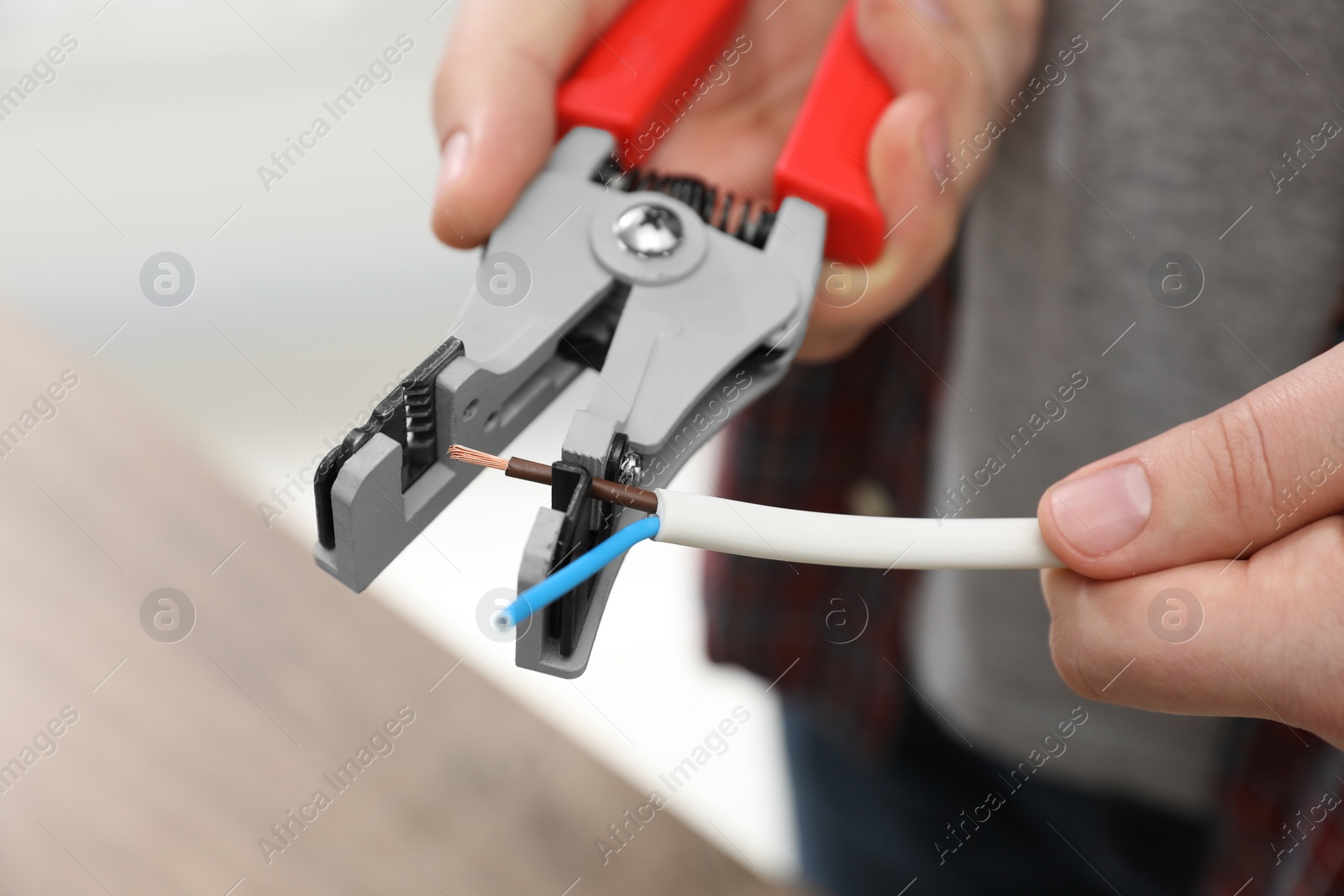 Photo of Professional electrician stripping wiring indoors, closeup view