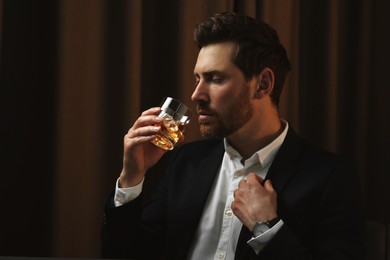 Man in suit drinking whiskey with ice cubes from glass on brown background