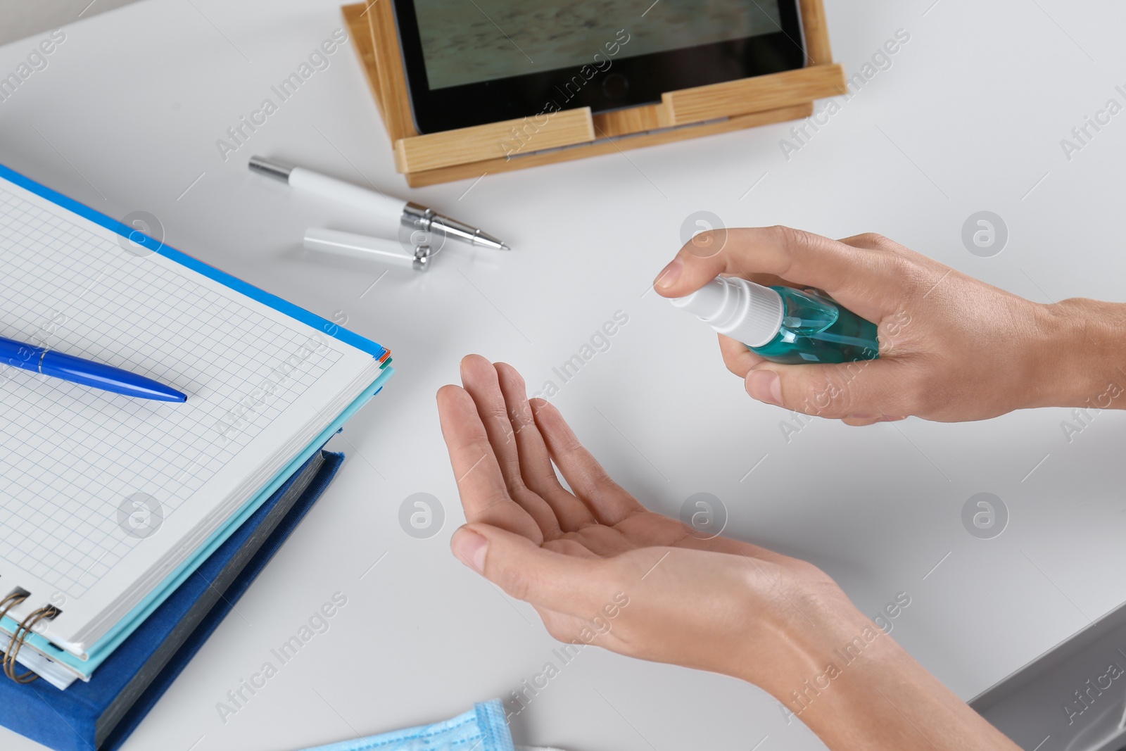 Photo of Woman applying hand sanitizer at white table in office, closeup. Personal hygiene during COVID-19 pandemic