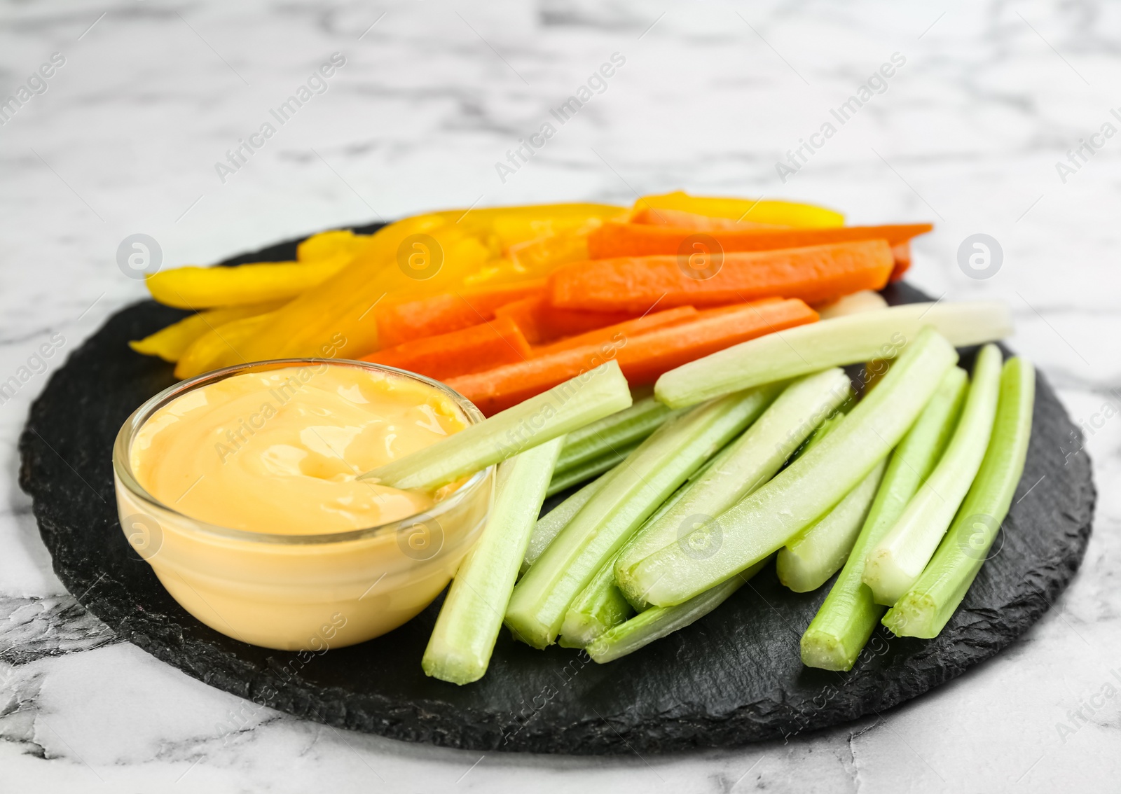 Photo of Celery and other vegetable sticks with dip sauce on white marble table