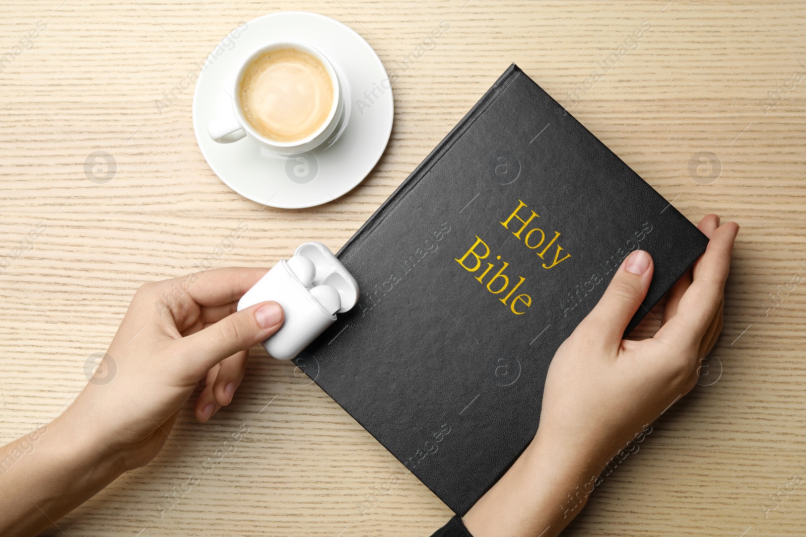 Photo of Woman with Bible, cup of coffee and earphones at wooden table, top view. Religious audiobook