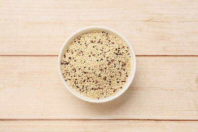 Photo of Raw quinoa seeds in bowl on wooden table, top view