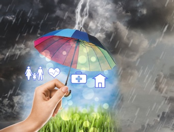 Image of Insurance agent protecting illustrations with rainbow umbrella from storm, closeup