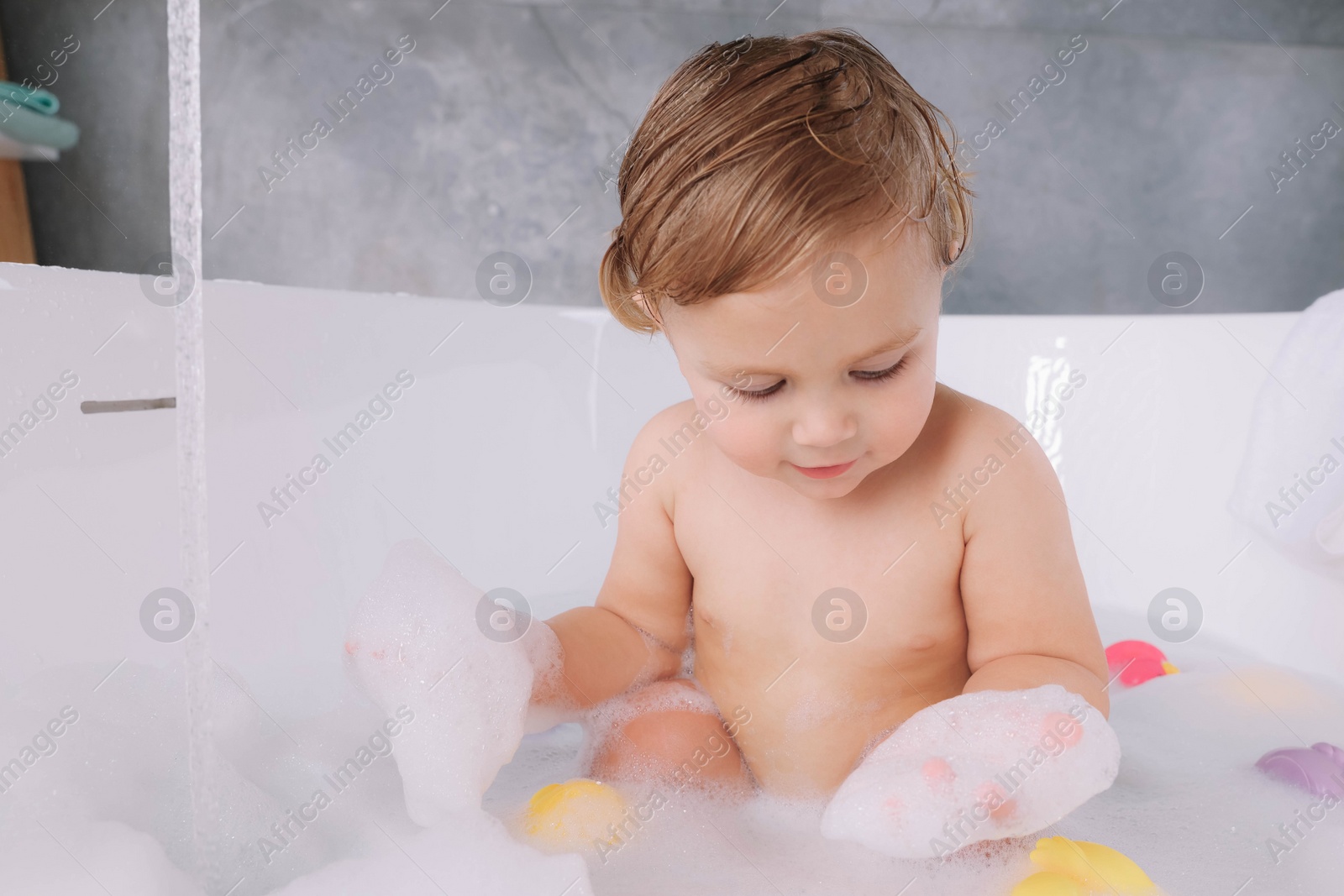 Photo of Cute little girl taking bubble bath with toys indoors