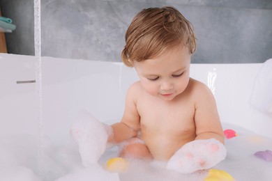 Cute little girl taking bubble bath with toys indoors