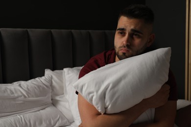 Sad man hugging pillow on bed at home. Space for text