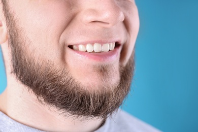 Young man with healthy teeth and beautiful smile on color background, closeup