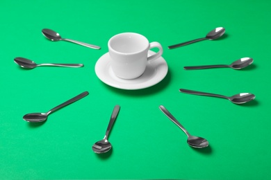 Photo of Empty cup and new teaspoons on green background