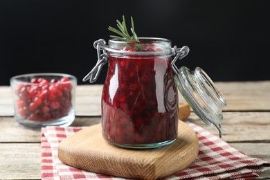 Photo of Fresh cranberry sauce in glass jar and rosemary on light wooden table