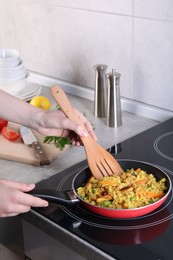 Photo of Woman frying rice with meat and vegetables on induction stove in kitchen, closeup