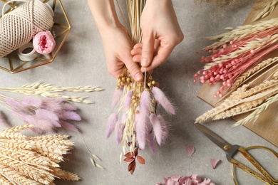 Photo of Florist making bouquet of dried flowers at grey stone table, top view