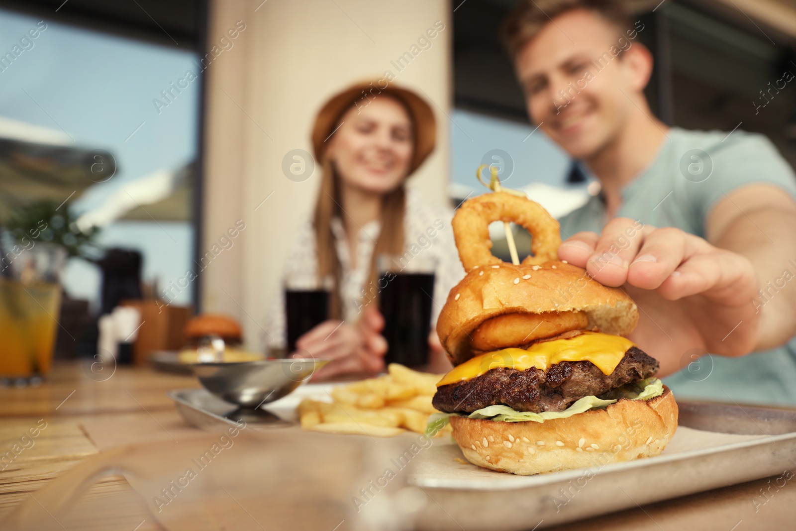 Photo of Young happy couple in street cafe, focus on man taking tasty burger. Space for text