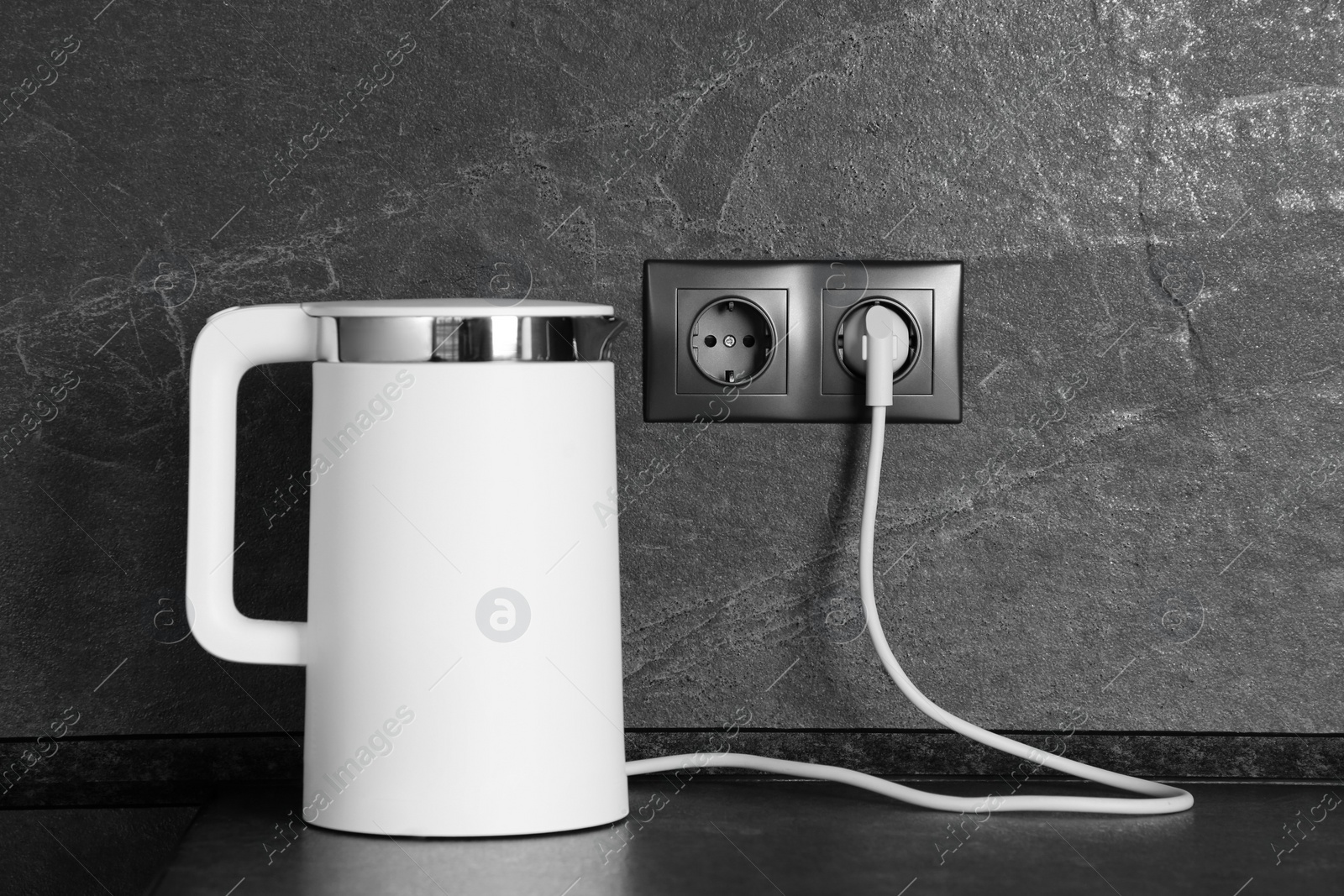 Photo of Electric kettle plugged into power socket on dark grey wall indoors