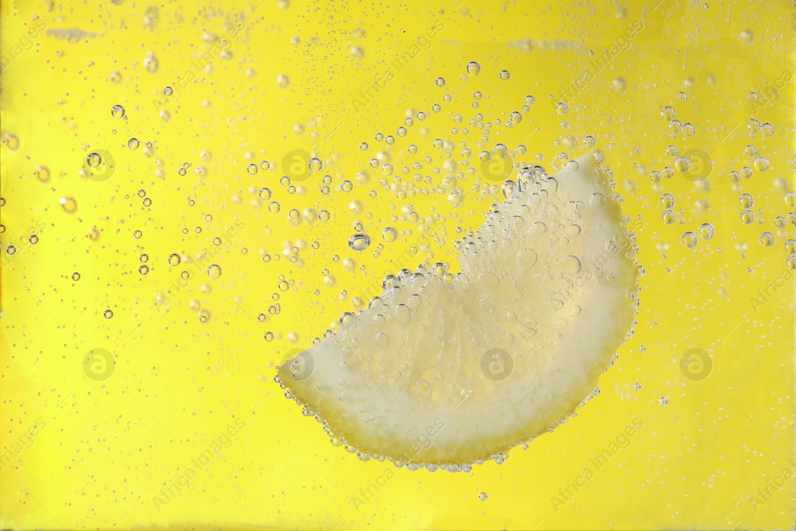 Photo of Juicy lemon slice in soda water against yellow background, closeup