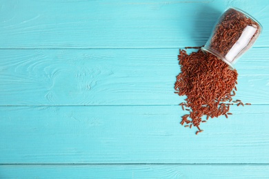 Jar with uncooked red rice on blue wooden background, top view. Space for text