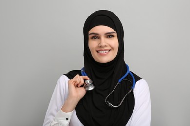 Photo of Muslim woman wearing hijab, medical uniform with stethoscope on light gray background