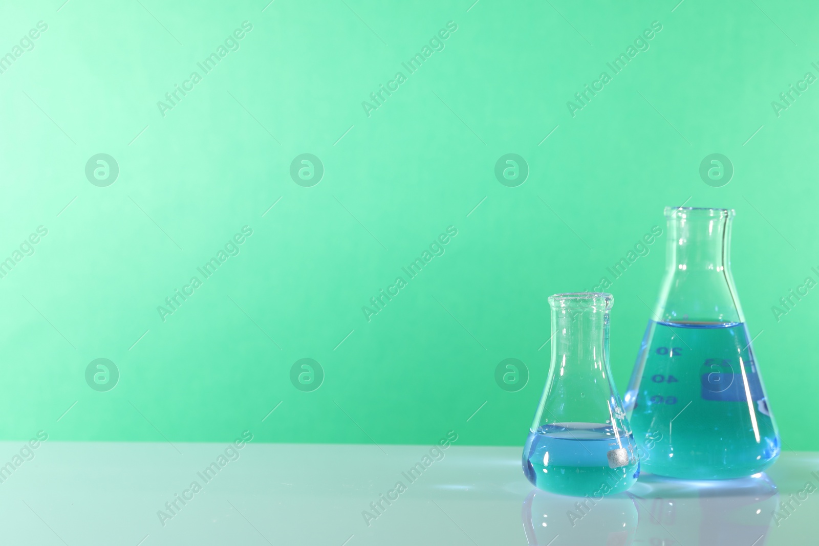 Photo of Laboratory analysis. Glass flasks on table against green background, space for text