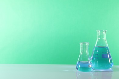 Laboratory analysis. Glass flasks on table against green background, space for text
