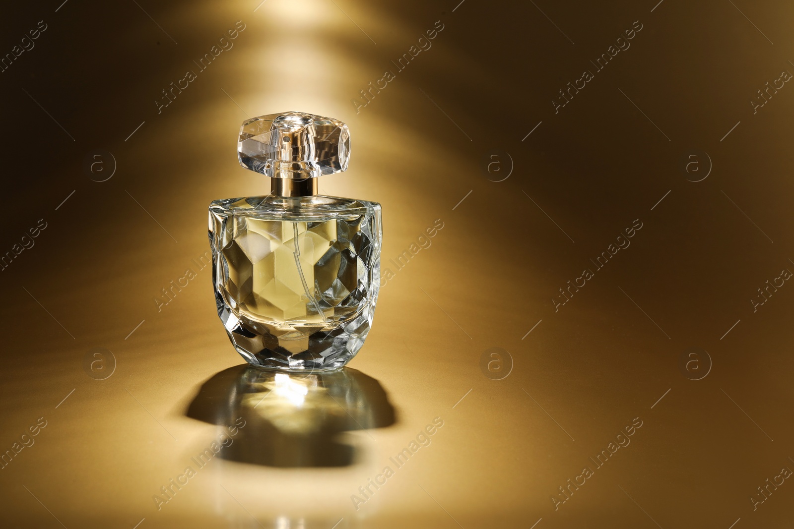 Photo of Luxury women's perfume. Sunlit glass bottle on golden background, space for text