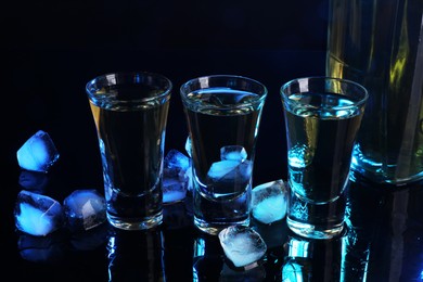 Photo of Alcohol drink in shot glasses, bottle and ice cubes on mirror surface