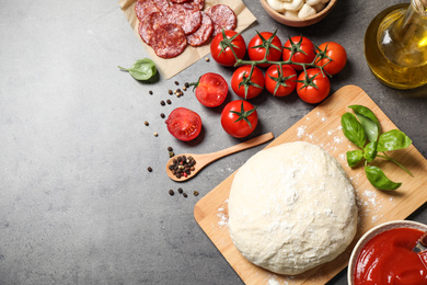 Flat lay composition with dough and ingredients on grey table, space for text. Pepperoni pizza recipe