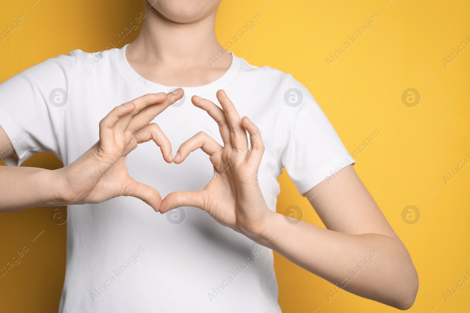 Photo of Woman making heart with hands on yellow background, closeup