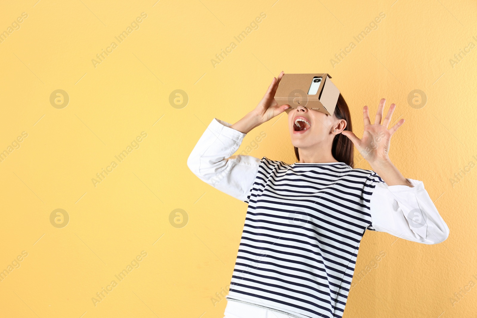 Photo of Young woman using cardboard virtual reality headset on color background. Space for text