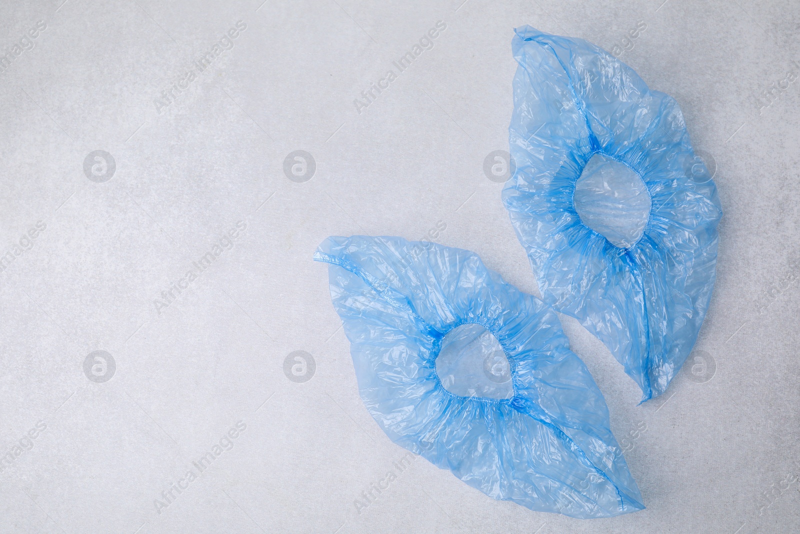 Photo of Pair of blue medical shoe covers on light grey background, top view. Space for text