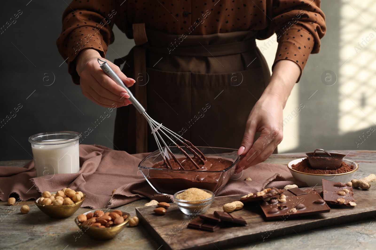 Photo of Woman mixing delicious chocolate cream with whisk at grey textured table, closeup