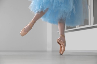 Ballerina in pointe shoes and light blue skirt dancing indoors, closeup