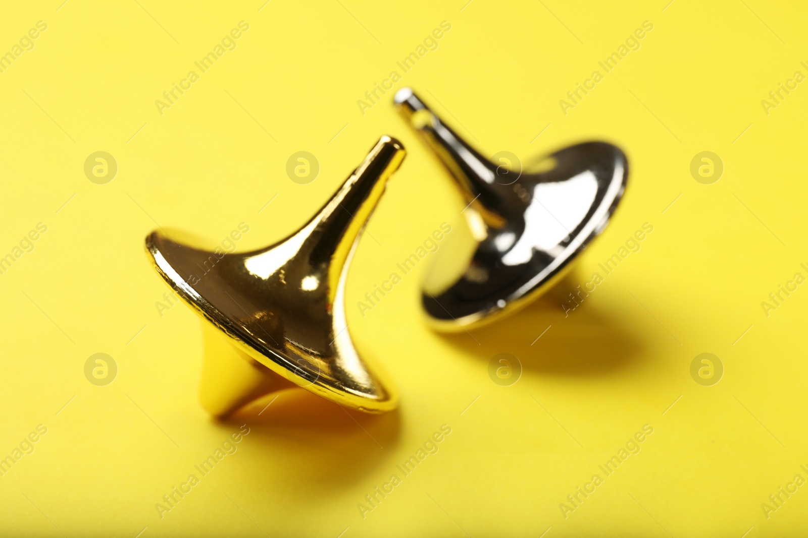 Photo of Golden and silver spinning tops on yellow background, closeup