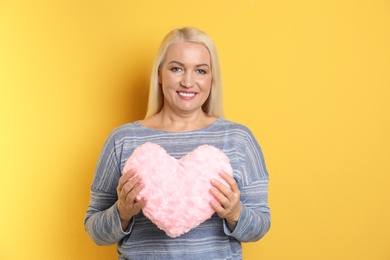 Photo of Portrait of mature woman with decorative heart shaped pillow on color background