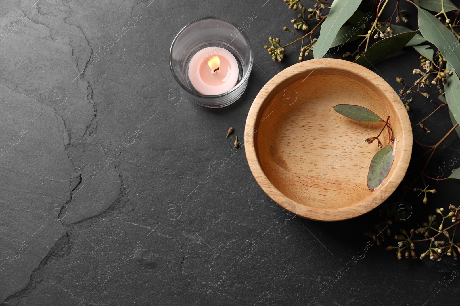 Photo of Wooden bowl, eucalyptus branches and burning candle on grey table, flat lay with space for text